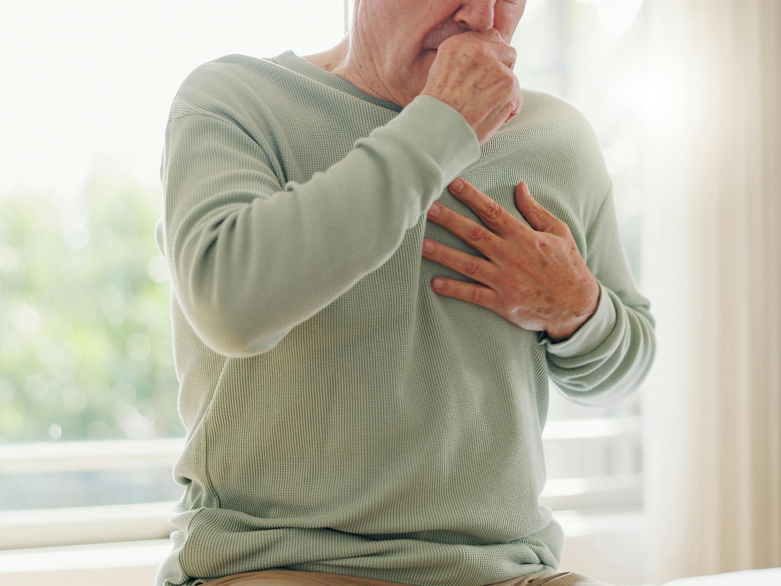 A man wearing a green shirt is coughing and clutching his chest